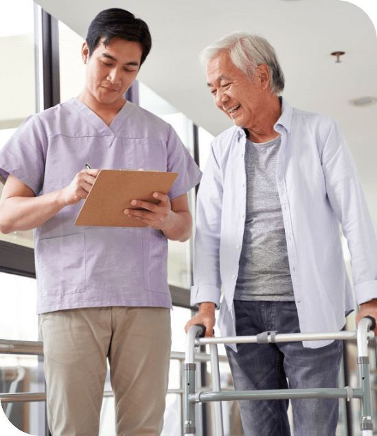 A nurse in scrubs and an elderly patient with a walker happily look at the information on a clipboard. 